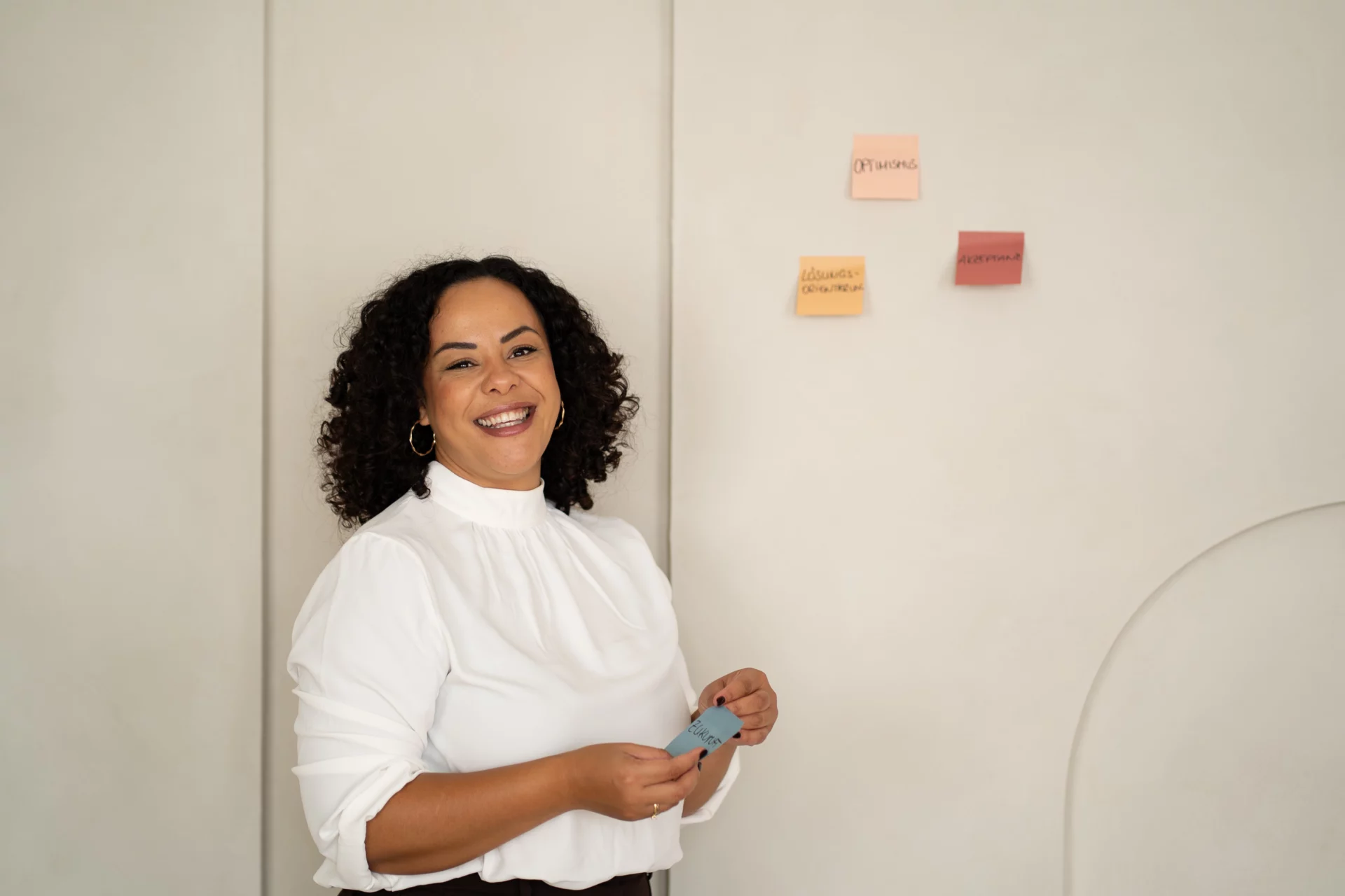 Olivia Simak steht lächelnd mit Moderationskarten vor einer Wand mit Notizzetteln